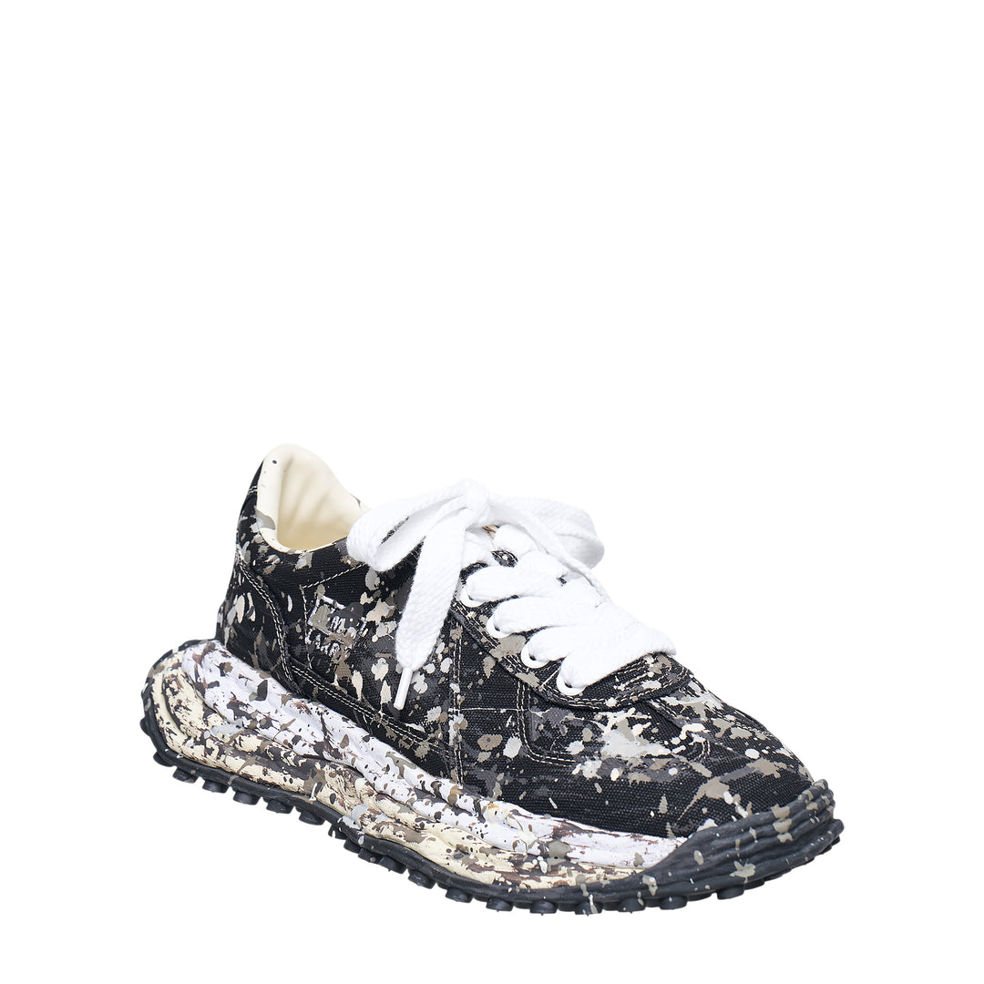 Mihara Yasuhiro Larry low-top sneaker in black canvas with white and grey paint-splatter sputtering finish across the upper and midsole, styled with flat white laces and a chunky lugged rubber outsole