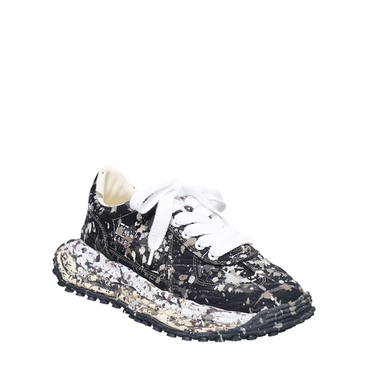 Mihara Yasuhiro Larry low-top sneaker in black canvas with white and grey paint-splatter sputtering finish across the upper and midsole, styled with flat white laces and a chunky lugged rubber outsole