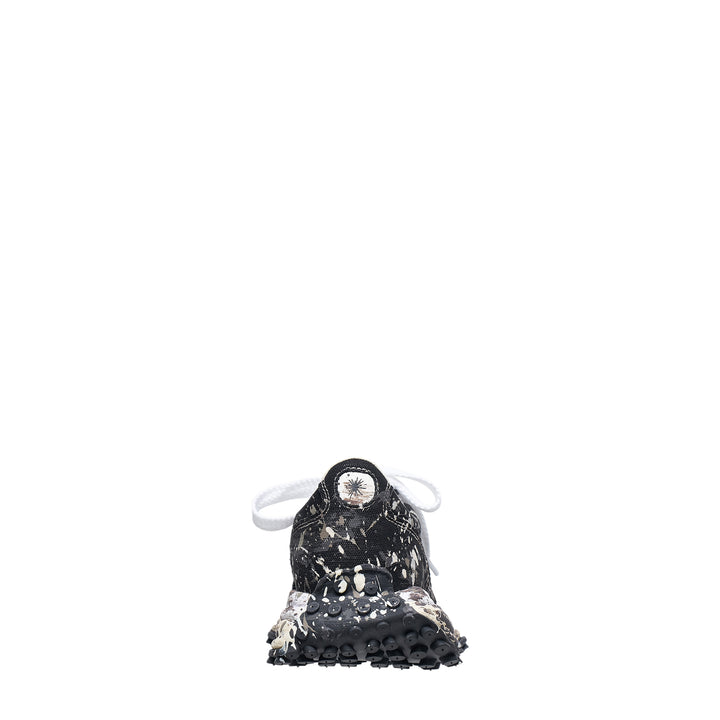 Mihara Yasuhiro Larry low-top sneaker in black canvas with white and grey paint-splatter sputtering finish across the upper and midsole, styled with flat white laces and a chunky lugged rubber outsole