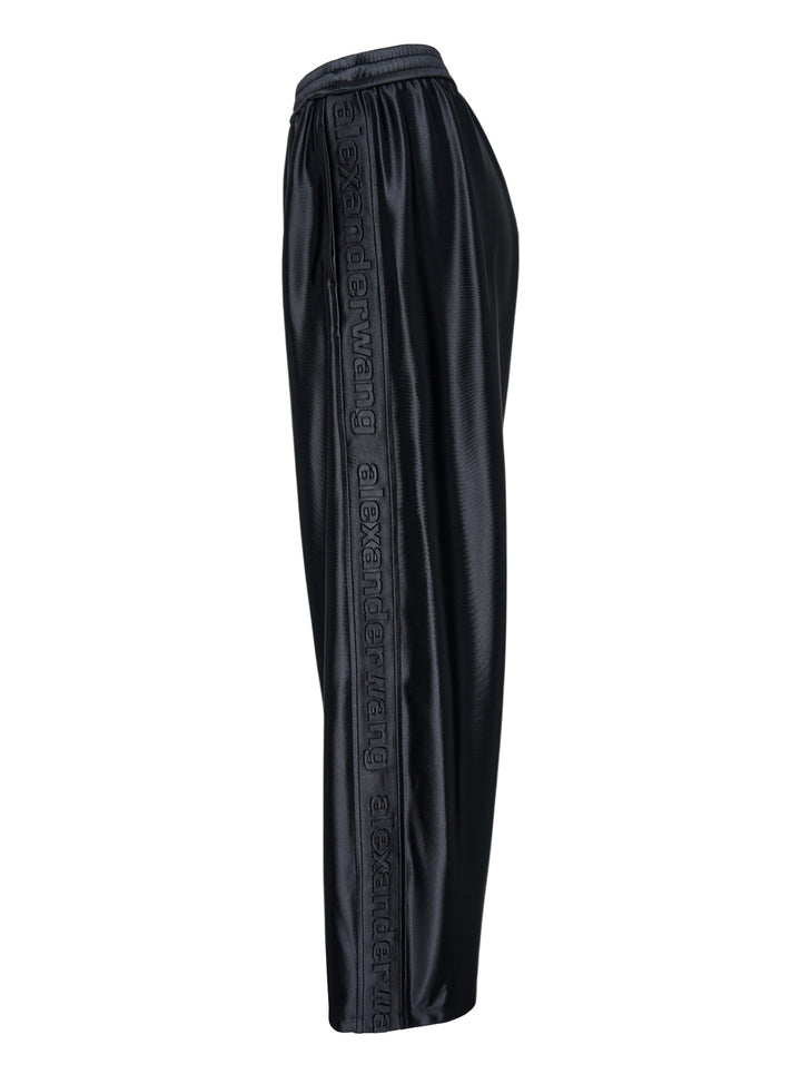 Alexander Wang mid-rise black glossy track pants with embossed side logo panels and elasticated waistband, shown from the front - view 3