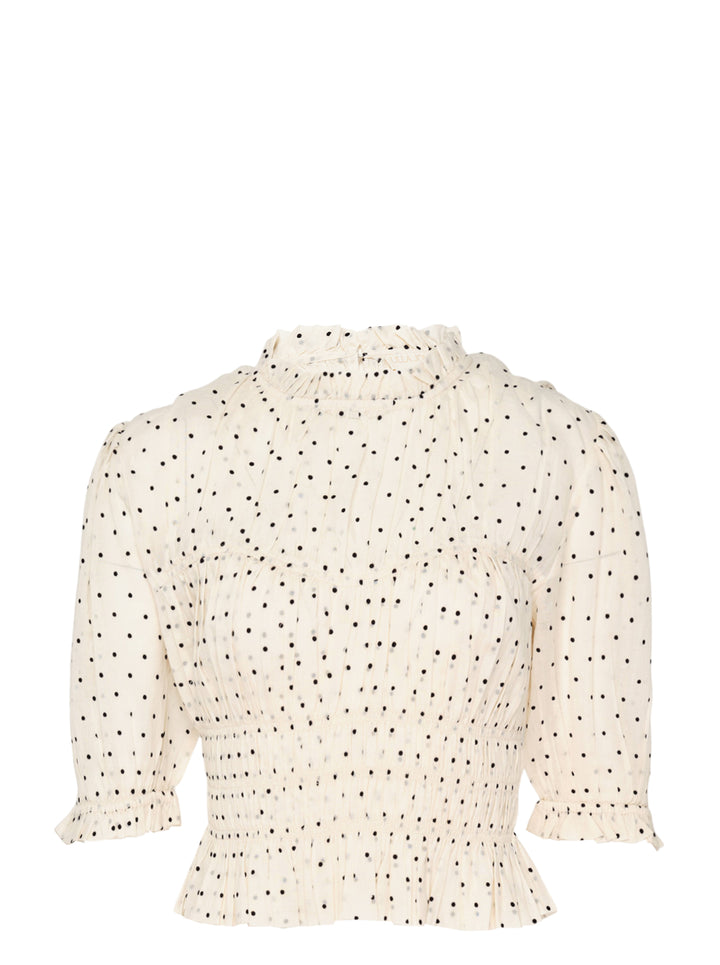 Ulla Johnson Rae short sleeve cotton top in ivory with black polka dots, featuring a ruffled high neckline, puffed sleeves with ruffle cuffs, smocked bodice, and a cropped peplum hem