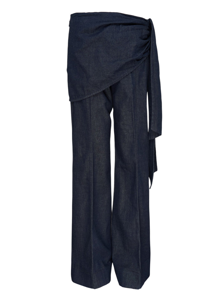 Zimmermann Draped Denim Flare Jeans in dark indigo, featuring a wide-leg silhouette with a wrap-style skirt overlay and self-tie gather detail at the hip