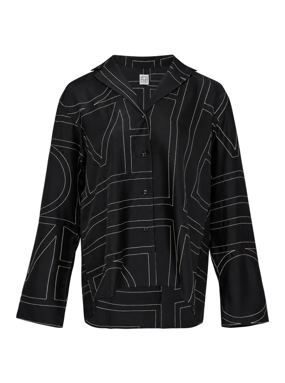 Totême Monogram Silk Pyjama Top in black, featuring all-over contrast-stitched monogram print, camp collar, partial button placket, and relaxed long-sleeve silhouette