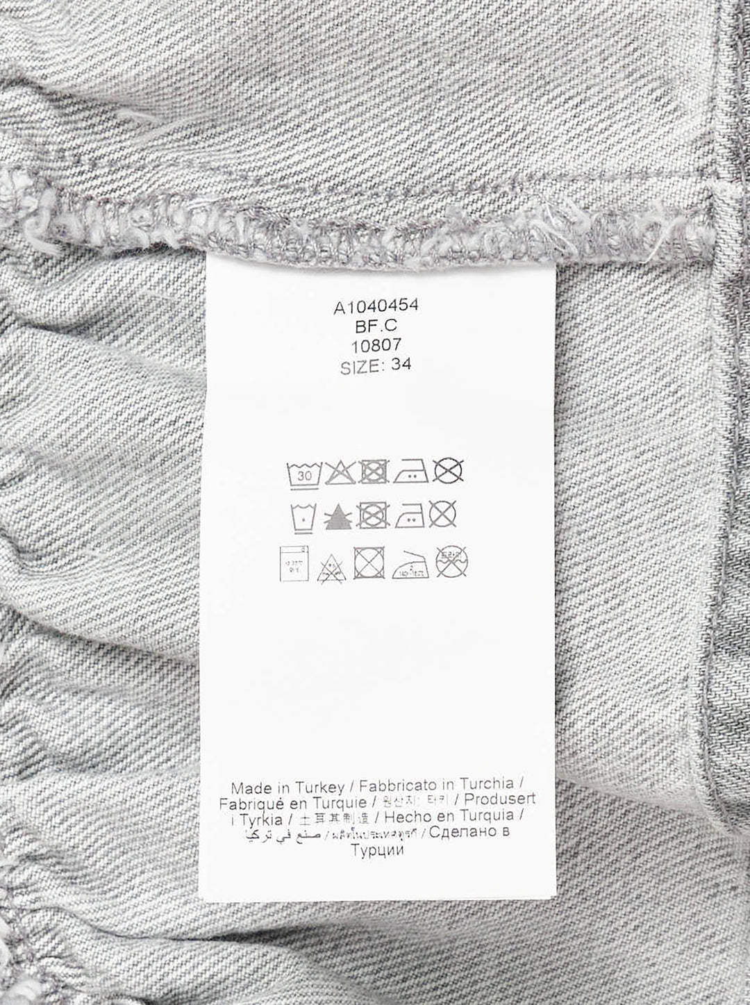 Ganni Rigid Denim Flounce Top in light grey wash, featuring a structured seamed bodice, three branded silver snap buttons at the centre front, wide shoulder straps, scoop neckline, and a gathered peplum ruffle hem - view 3