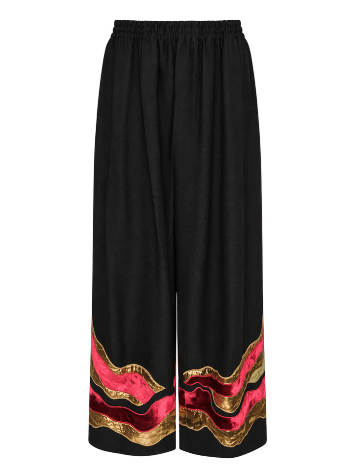 Biyan black gabardine wide leg pants with layered wavy velvet and gold metallic appliqué trim at the hem, elastic waistband, front view on white background