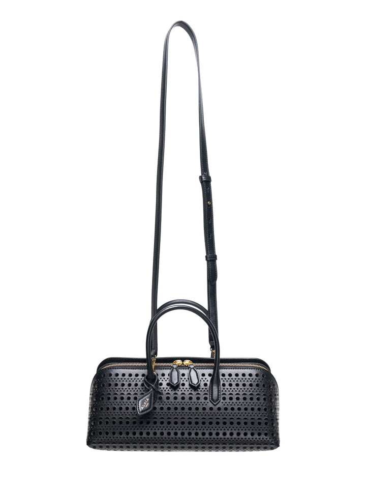 Alaïa Delta S top handle bag in black perforated leather with circular and triangular cutout pattern, dual rolled handles, gold-tone zip closure, and a long adjustable crossbody strap, shown on a white background