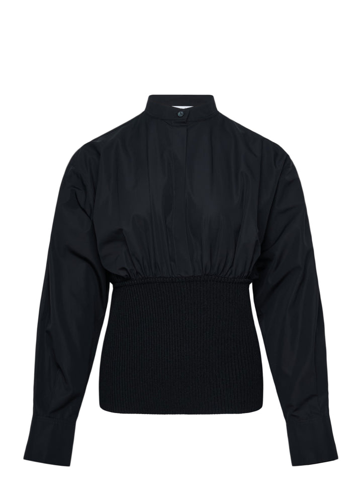 Alaïa Cinched Cotton Poplin Shirt in black, featuring a voluminous poplin upper, mandarin collar with button fastening, long sleeves, and a structured ribbed knit cinched waistband