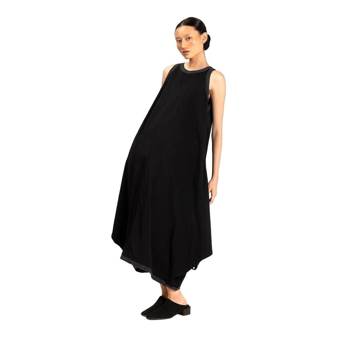 Model wearing an Anaabu black sleeveless midi dress with a voluminous A-line silhouette, asymmetric handkerchief hemline, and fine metallic stud trim at the neckline and hem - packshot