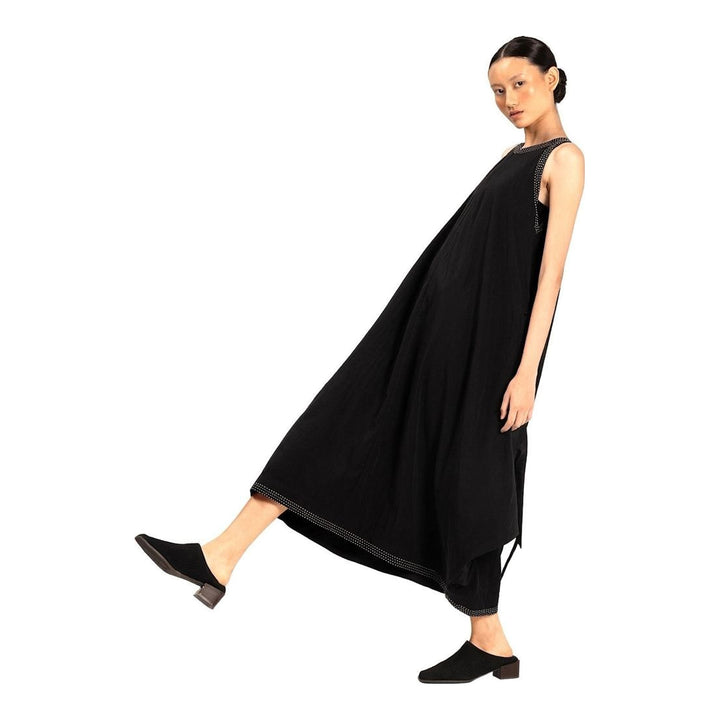 Model wearing an Anaabu black sleeveless midi dress with a voluminous A-line silhouette, asymmetric handkerchief hemline, and fine metallic stud trim at the neckline and hem - packshot