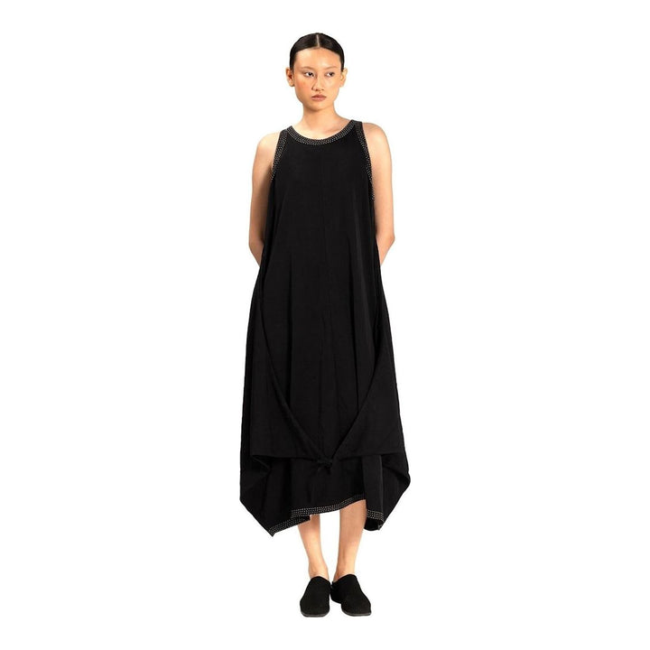 Model wearing an Anaabu black sleeveless midi dress with a voluminous A-line silhouette, asymmetric handkerchief hemline, and fine metallic stud trim at the neckline and hem - packshot