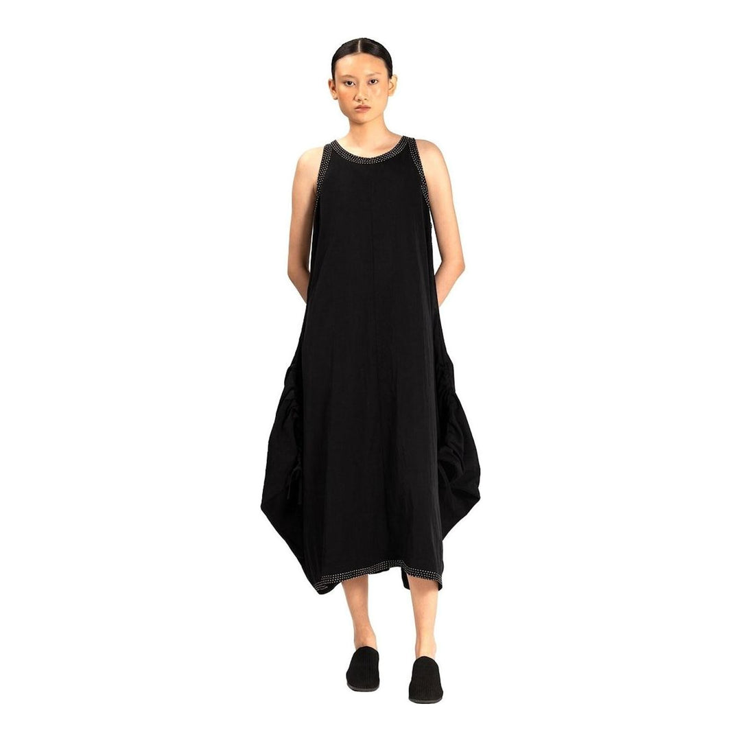 Model wearing an Anaabu black sleeveless midi dress with a voluminous A-line silhouette, asymmetric handkerchief hemline, and fine metallic stud trim at the neckline and hem - packshot