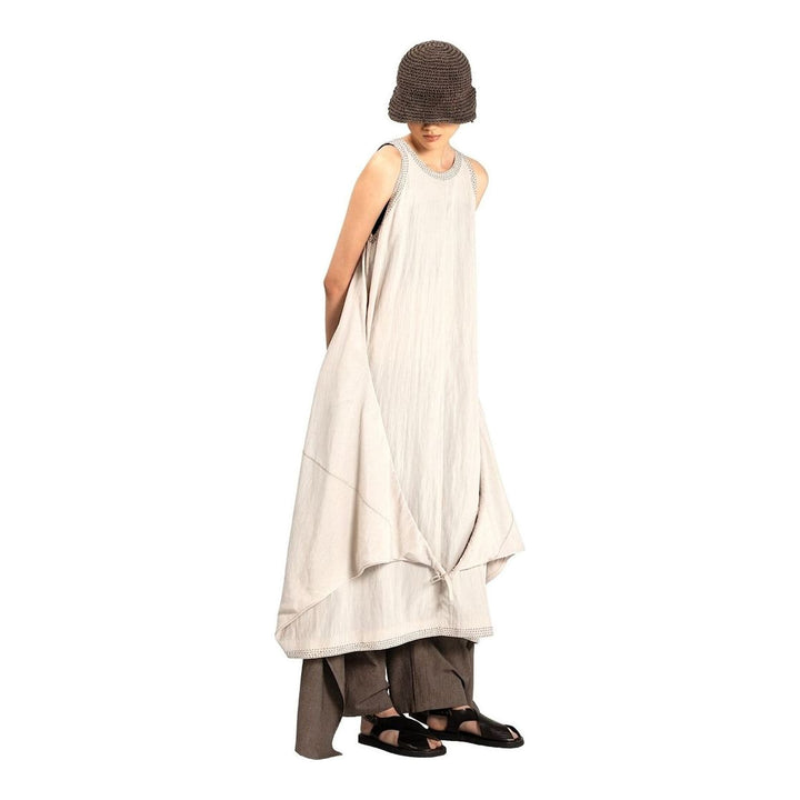 Model wearing an Anaabu black sleeveless midi dress with a voluminous A-line silhouette, asymmetric handkerchief hemline, and fine metallic stud trim at the neckline and hem - packshot