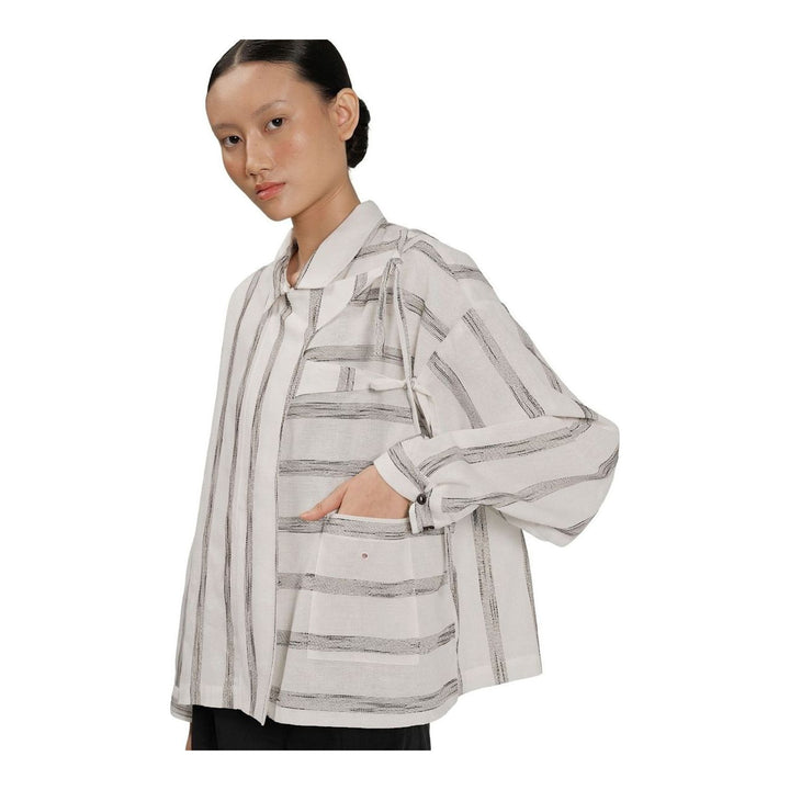 Model wearing Anaabu Asymmetrical Batwing Top in black textured fabric with an open collar, asymmetric front placket, patch chest pocket, and long batwing sleeves, styled with dark drop-crotch trousers and brown mules - packshot