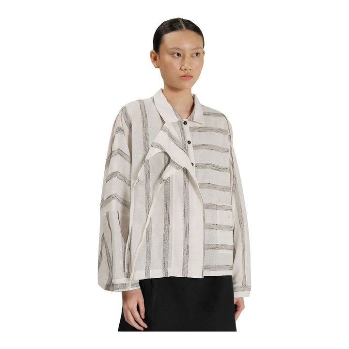 Model wearing Anaabu Asymmetrical Batwing Top in black textured fabric with an open collar, asymmetric front placket, patch chest pocket, and long batwing sleeves, styled with dark drop-crotch trousers and brown mules - packshot
