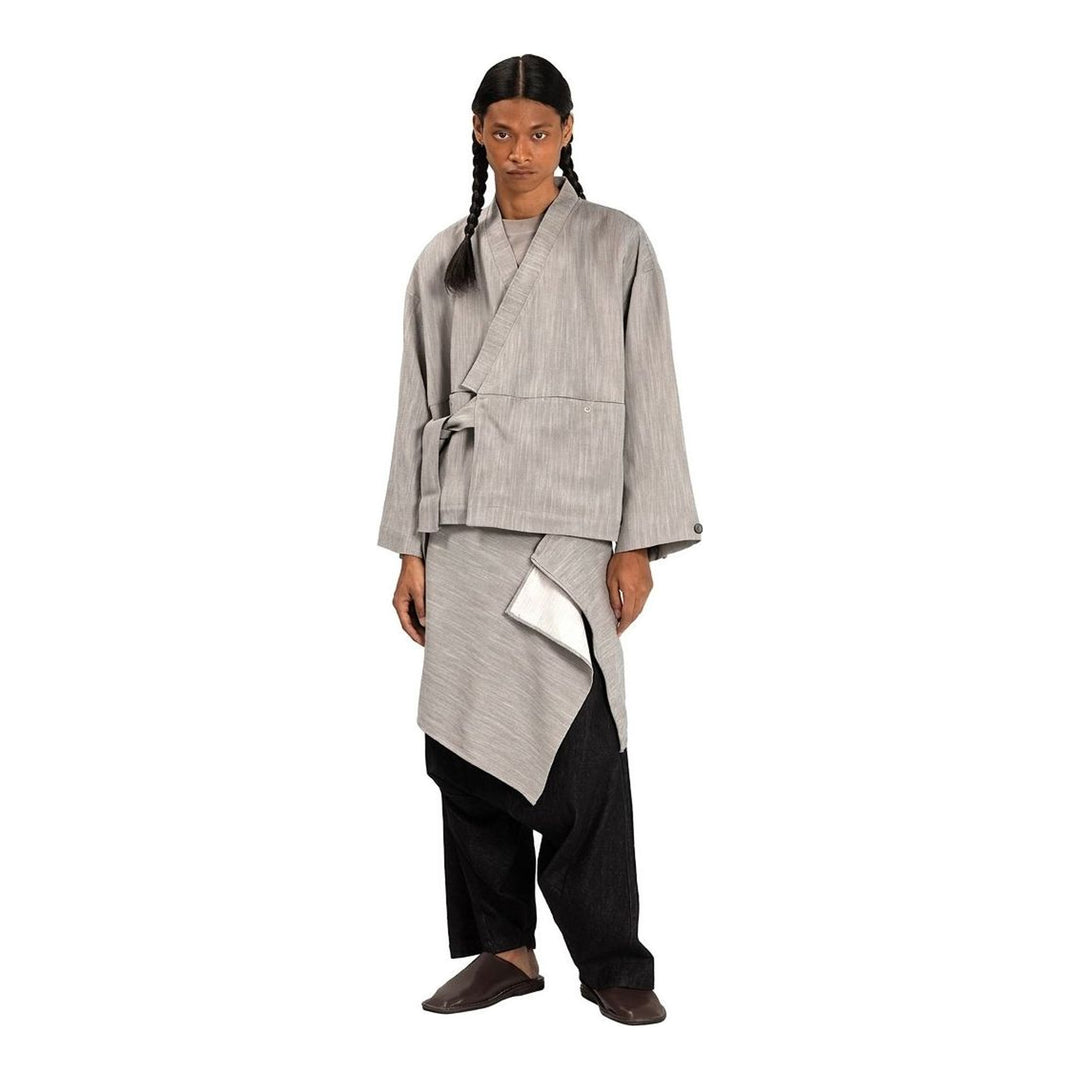 Model wearing the Anaabu Shawl Jacket in black — a draped wrap-style jacket with oversized shawl collar and self-tie belt, styled over a black turtleneck and olive wide-leg trousers - packshot