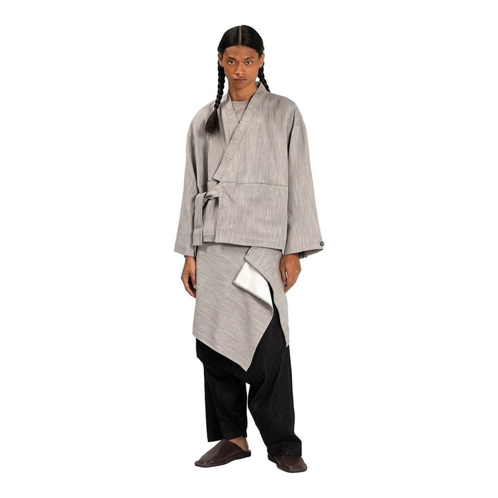 Model wearing the Anaabu Shawl Jacket in black — a draped wrap-style jacket with oversized shawl collar and self-tie belt, styled over a black turtleneck and olive wide-leg trousers - packshot