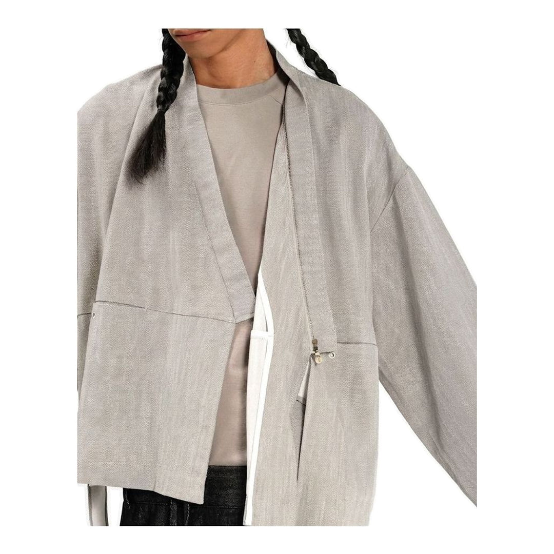 Model wearing the Anaabu Shawl Jacket in black — a draped wrap-style jacket with oversized shawl collar and self-tie belt, styled over a black turtleneck and olive wide-leg trousers - packshot