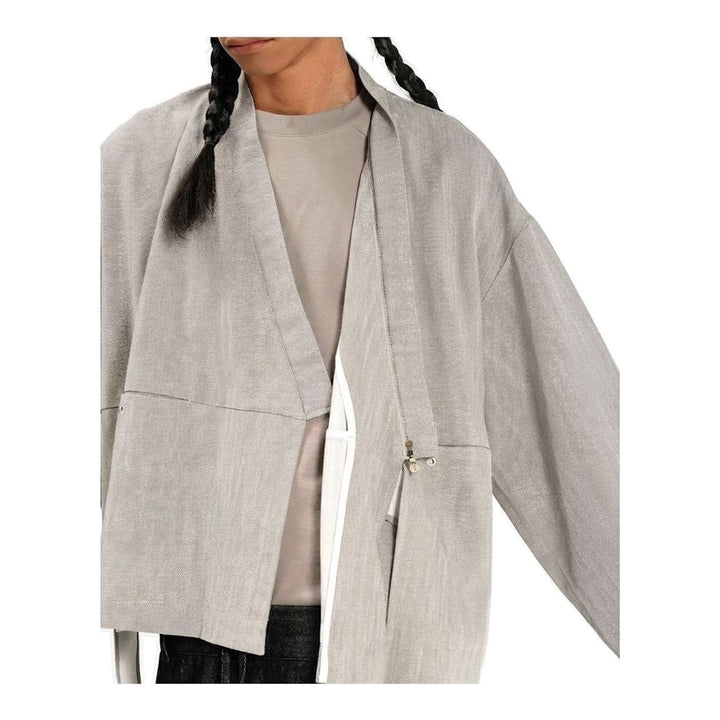 Model wearing the Anaabu Shawl Jacket in black — a draped wrap-style jacket with oversized shawl collar and self-tie belt, styled over a black turtleneck and olive wide-leg trousers - packshot