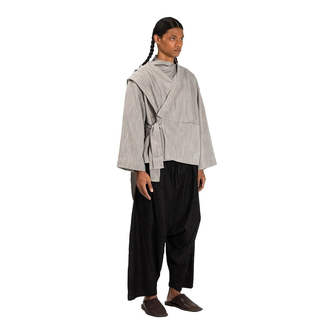 Model wearing the Anaabu Shawl Jacket in black — a draped wrap-style jacket with oversized shawl collar and self-tie belt, styled over a black turtleneck and olive wide-leg trousers - packshot