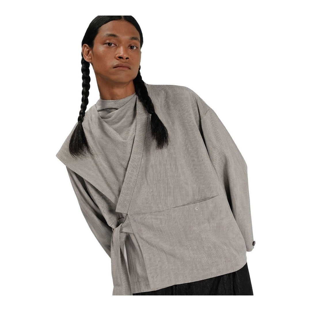 Model wearing the Anaabu Shawl Jacket in black — a draped wrap-style jacket with oversized shawl collar and self-tie belt, styled over a black turtleneck and olive wide-leg trousers - packshot