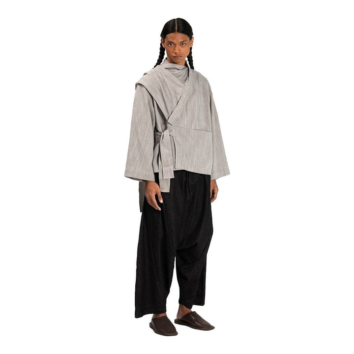 Model wearing the Anaabu Shawl Jacket in black — a draped wrap-style jacket with oversized shawl collar and self-tie belt, styled over a black turtleneck and olive wide-leg trousers - packshot