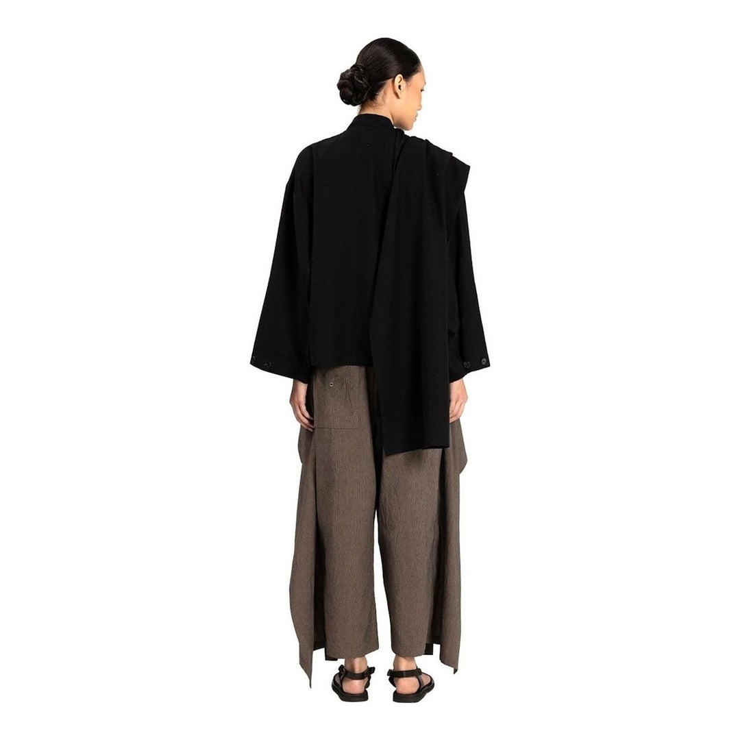 Model wearing the Anaabu Shawl Jacket in black — a draped wrap-style jacket with oversized shawl collar and self-tie belt, styled over a black turtleneck and olive wide-leg trousers - packshot