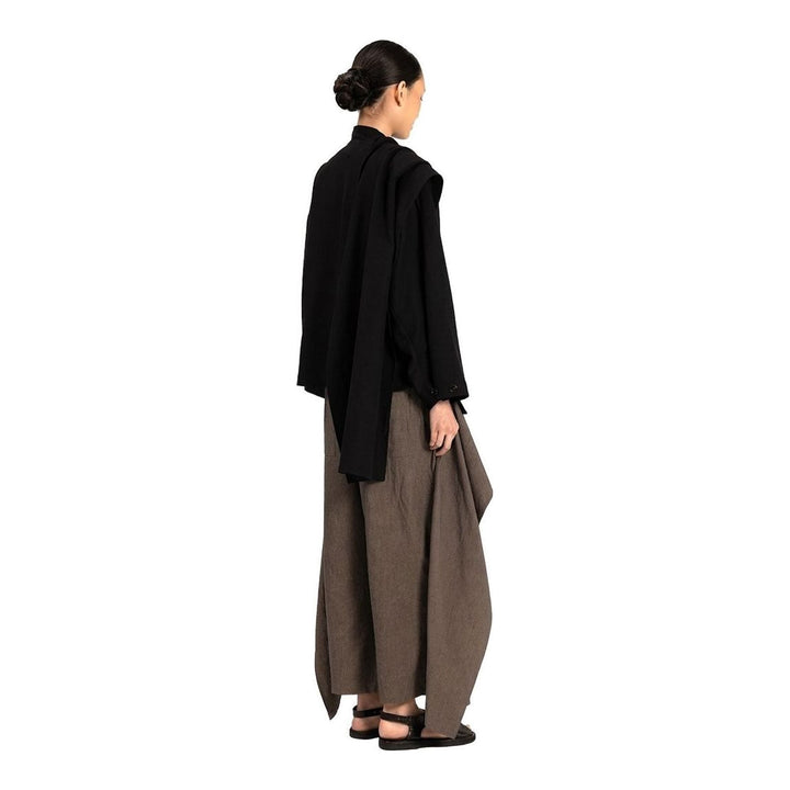 Model wearing the Anaabu Shawl Jacket in black — a draped wrap-style jacket with oversized shawl collar and self-tie belt, styled over a black turtleneck and olive wide-leg trousers - packshot
