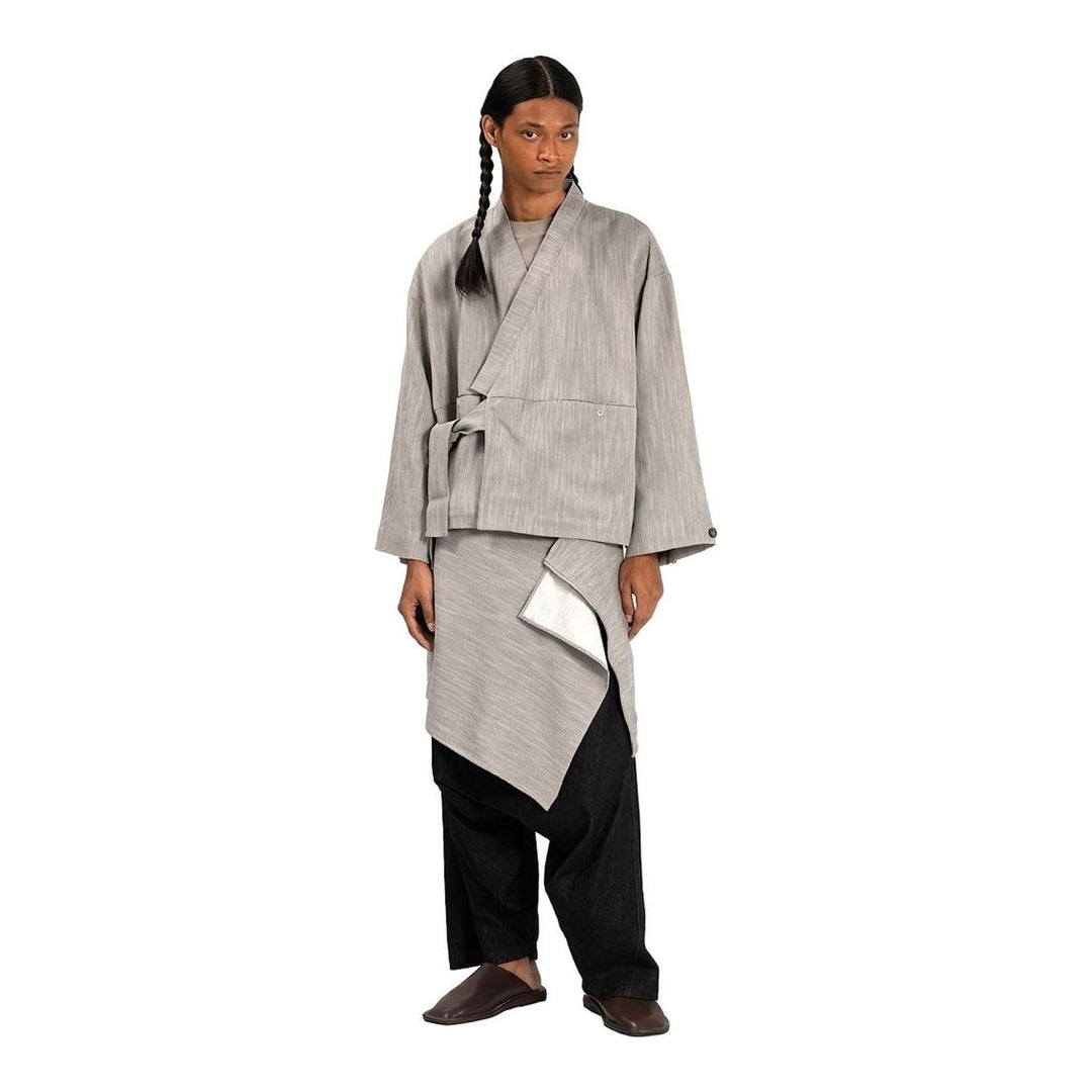 Model wearing the Anaabu Shawl Jacket in black — a draped wrap-style jacket with oversized shawl collar and self-tie belt, styled over a black turtleneck and olive wide-leg trousers - packshot