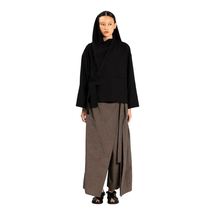 Model wearing the Anaabu Shawl Jacket in black — a draped wrap-style jacket with oversized shawl collar and self-tie belt, styled over a black turtleneck and olive wide-leg trousers - packshot