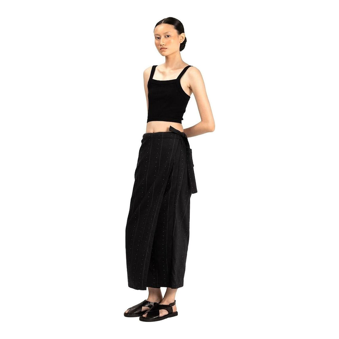 Model wearing Anaabu The Skants — black wide-leg cropped pants with large draped overlay panels featuring pinstripe and dot print, paired with a black square-neck crop top and leather sandals - packshot