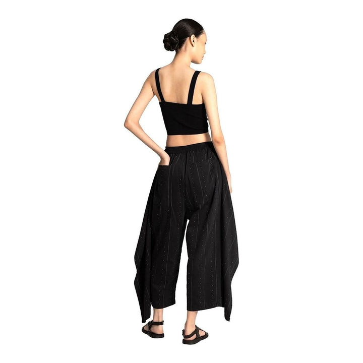 Model wearing Anaabu The Skants — black wide-leg cropped pants with large draped overlay panels featuring pinstripe and dot print, paired with a black square-neck crop top and leather sandals - packshot
