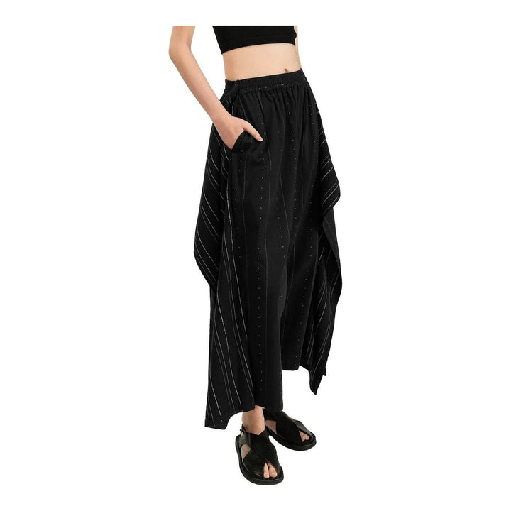 Model wearing Anaabu The Skants — black wide-leg cropped pants with large draped overlay panels featuring pinstripe and dot print, paired with a black square-neck crop top and leather sandals - packshot