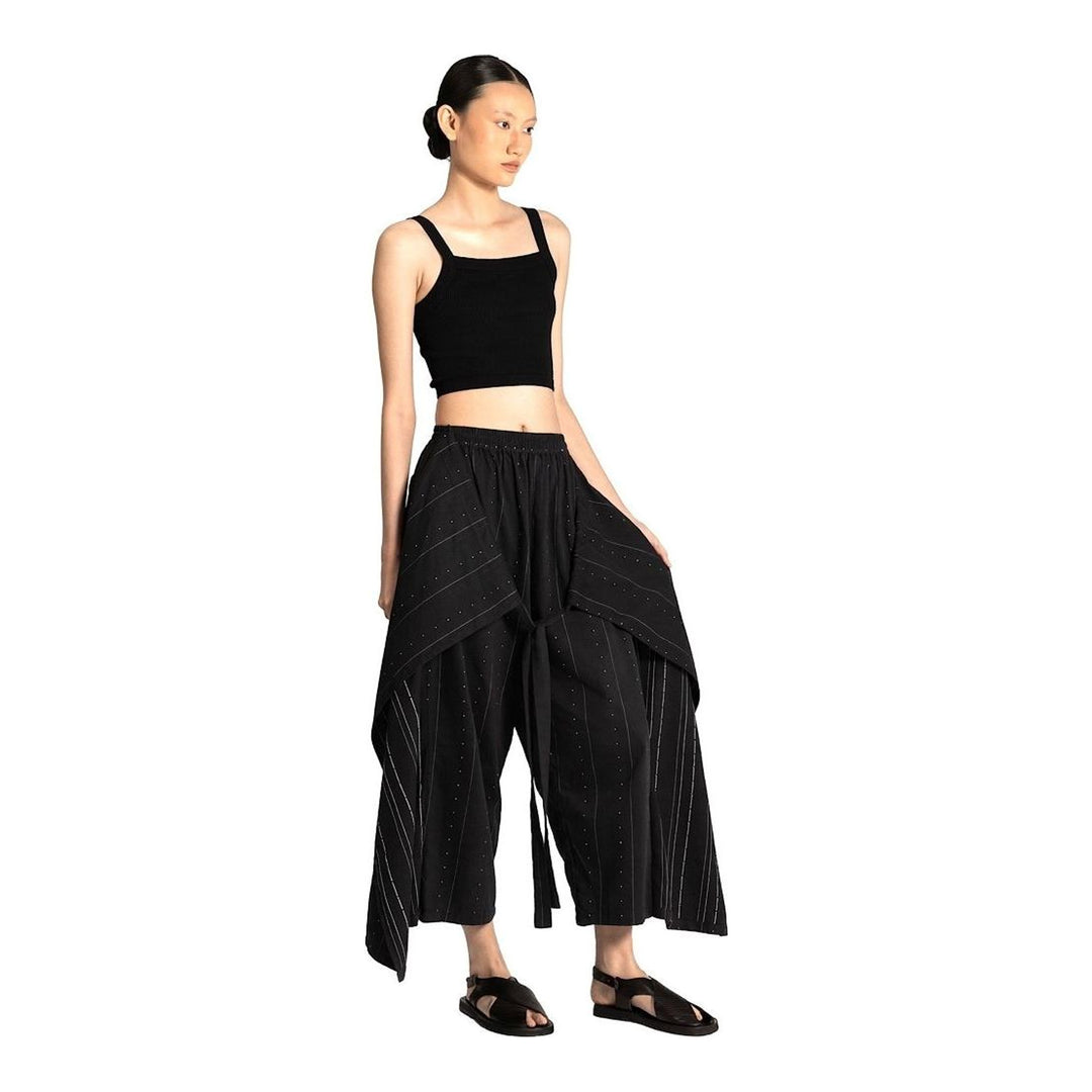 Model wearing Anaabu The Skants — black wide-leg cropped pants with large draped overlay panels featuring pinstripe and dot print, paired with a black square-neck crop top and leather sandals - packshot