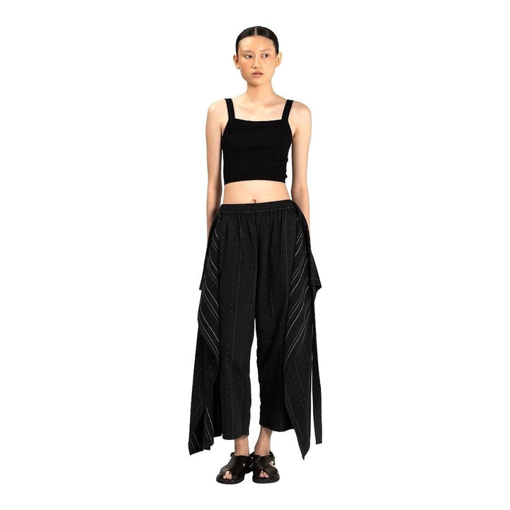 Model wearing Anaabu The Skants — black wide-leg cropped pants with large draped overlay panels featuring pinstripe and dot print, paired with a black square-neck crop top and leather sandals - packshot