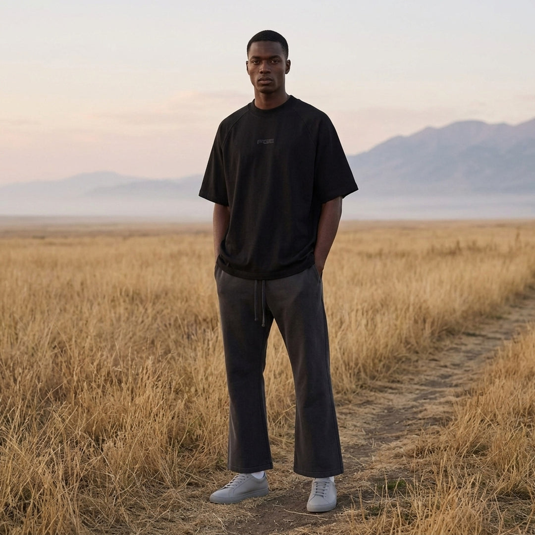 Fear of God Essentials Essential Raglan Tee in black with tonal FGE logo on the chest and ribbed crewneck, shown flat from the front - lifestyle