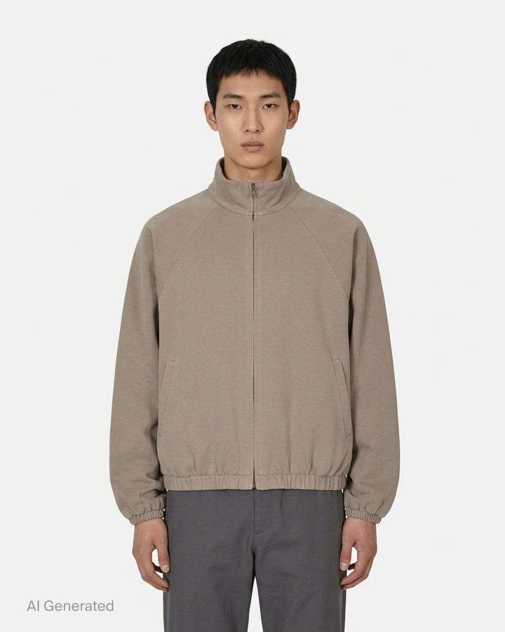 Fear of God Essentials Modern Filled Blouson Jacket in taupe, featuring a full-length zip, stand collar, raglan sleeves, and elasticated hem and cuffs, shown flat on a white background - front