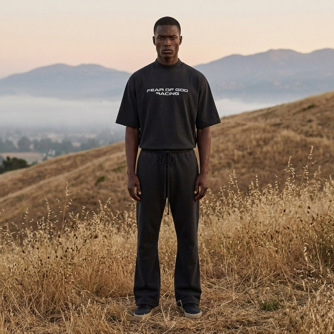 Fear of God Essentials Racing Panelled Modern Tee in black with a mock neck, oversized short sleeves, tiered hem and grey "Fear of God Racing" graphic on the chest - lifestyle