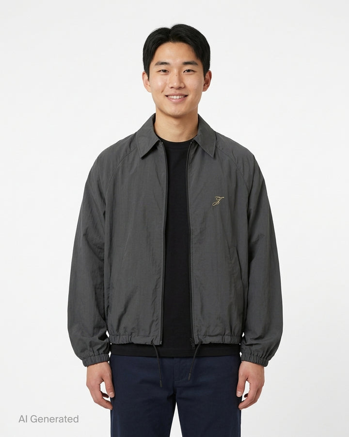 Jacquemus Le Coupe-Vent charcoal grey zip-up windbreaker with collar, elasticated cuffs and hem, and embroidered gold monogram on the chest - front