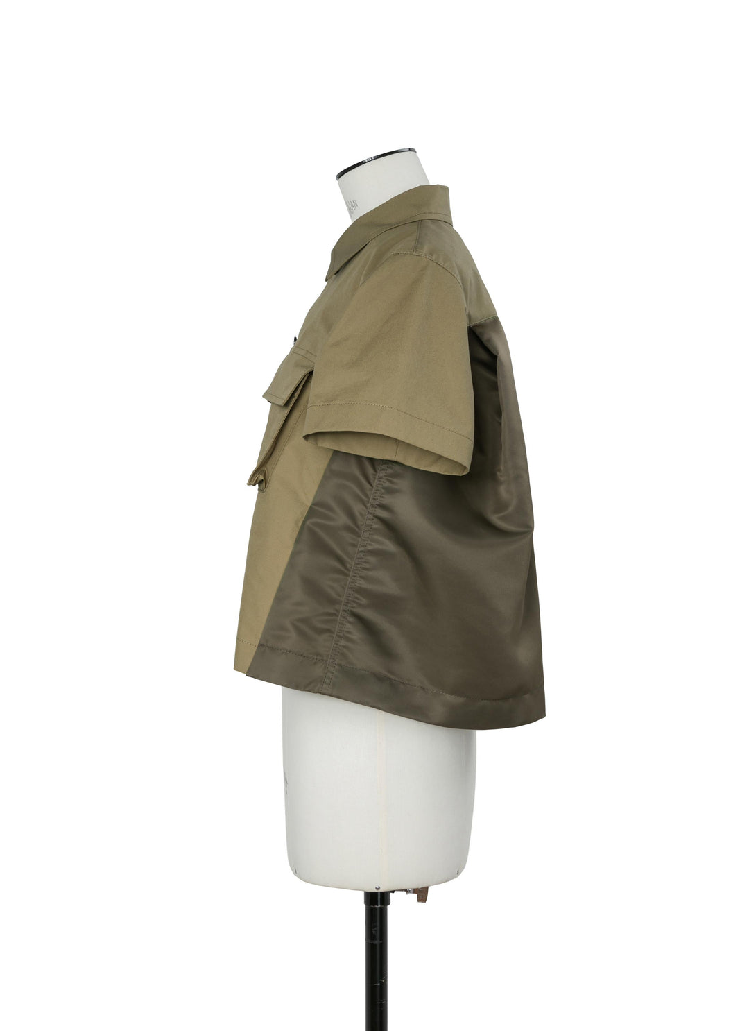 side view of sacai khaki cropped cotton weather shirt showing the trapeze swing silhouette and olive nylon back panel, on a dress form