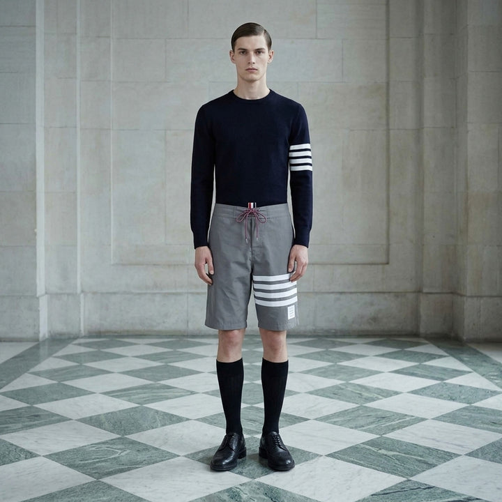 Thom Browne grey board shorts with 4-bar white stripe detail on one leg, red and white braided drawstring waist, and woven logo label at the hem - lifestyle