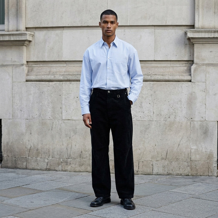 Wooyoungmi black corduroy wide-leg pants with elasticated waistband, buckle hardware, articulated knee panels, and cuffed hems, displayed flat on a white background - lifestyle
